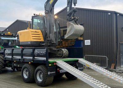 NUMAC 12T drop side trailer with a digger on top being unloaded.